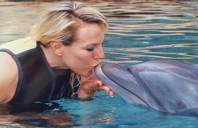 A woman kissing a dolphin