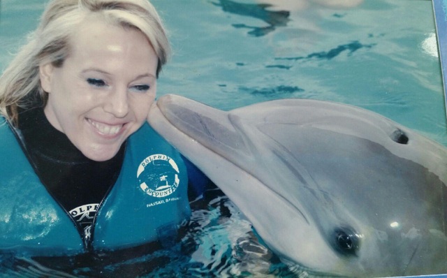 A woman smiles as she swims with a dolphin.